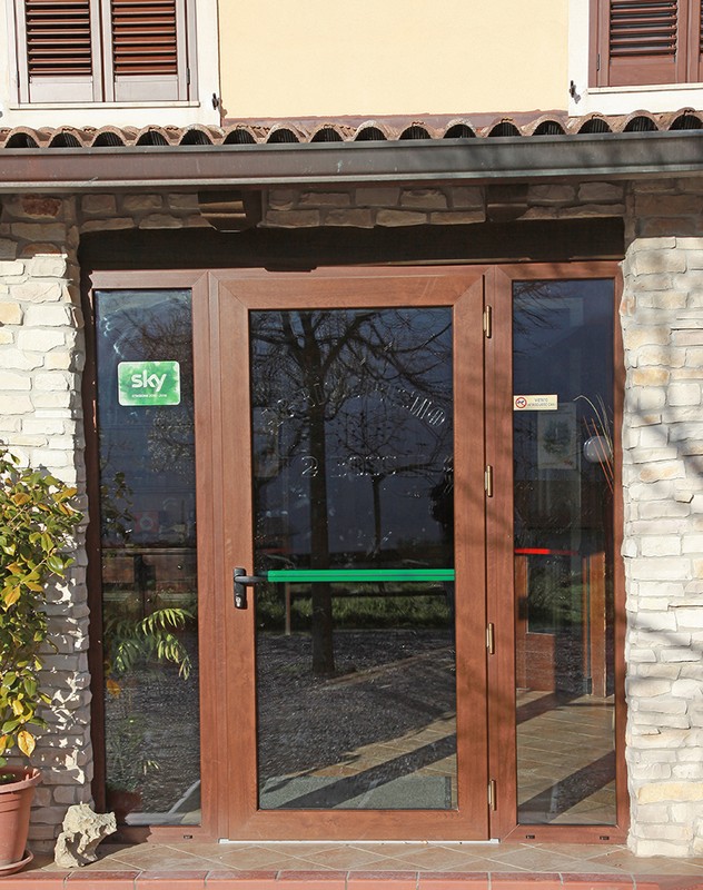 Tipologia serramenti: Porta d’ingresso con Maniglione Antipanico - Apertura: Esterna - Profilo PVC: Geneo - Colore: Noce - Accessori: Bronzo